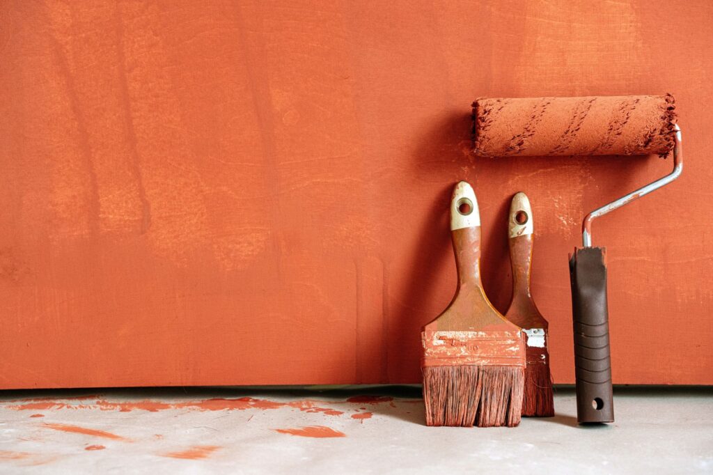 Close-up of paint rollers and brushes with orange paint against a painted wall, when to use waterproofing instead of paint