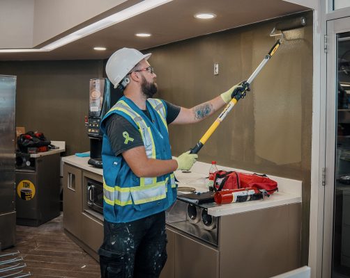 Commercial painter using an extension roller to paint an interior wall of a retail premises