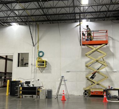 Industrial painter using a scissor lift to paint a warehouse interior wall