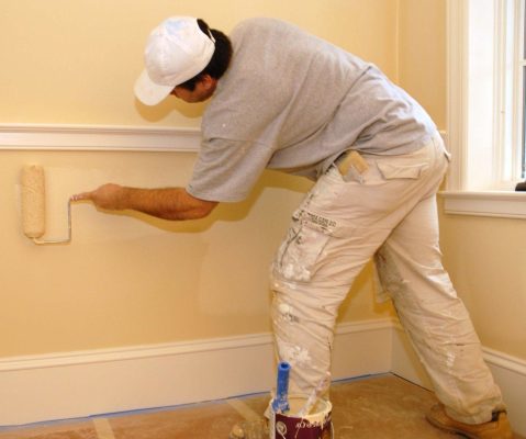Residential painter applying paint with a roller to an interior wall