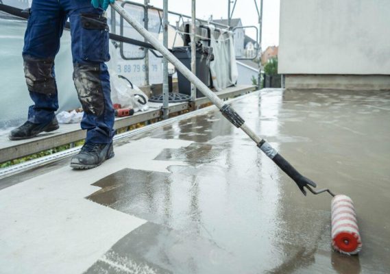 Worker applying a waterproofing membrane to a concrete surface using a roller